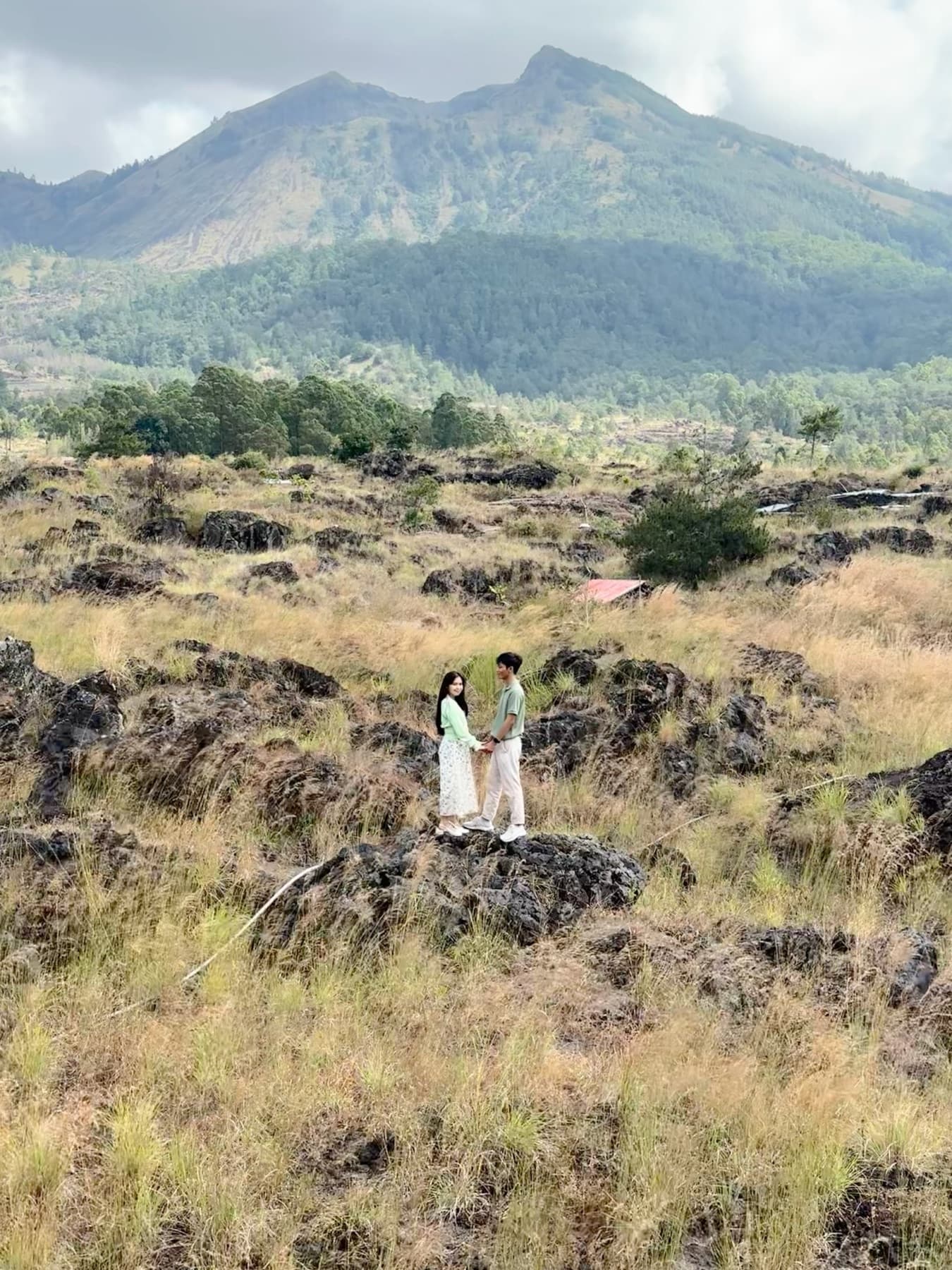 Ima and Sadu holding hands on black volcanic rocks below Mount Batur