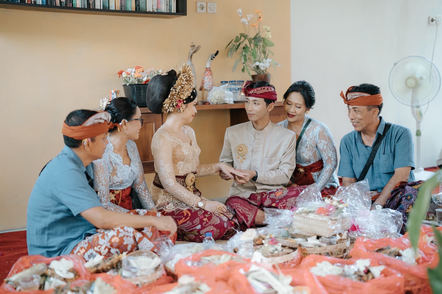 Ima and Sadu holding hands, surrounded by both families sitting on the floor