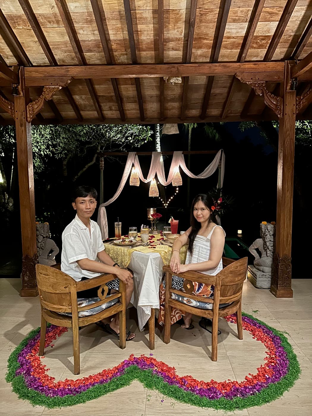 Ima and Sadu at a candlelit dinner table, with a heart made of flower petals on the floor